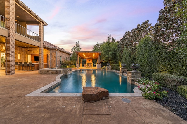 pool at dusk with a patio, an outdoor stone fireplace, a pool with connected hot tub, and outdoor dry bar