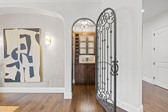 hallway featuring wood finished floors, arched walkways, and baseboards