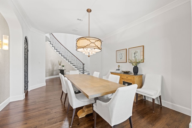 dining room featuring dark wood-style floors, arched walkways, ornamental molding, stairs, and a chandelier