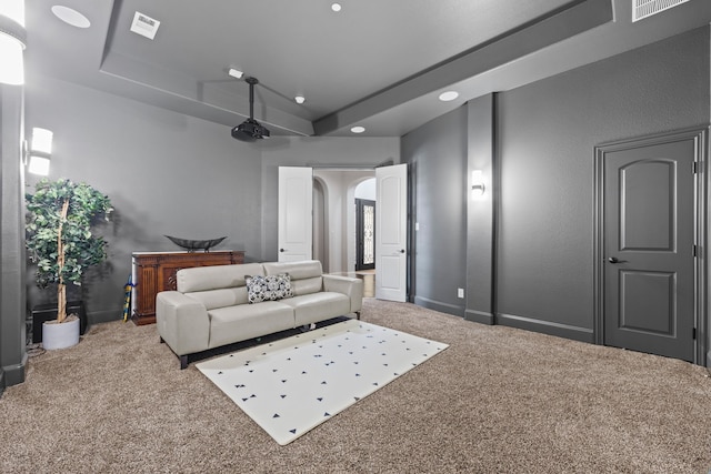 carpeted living room with visible vents, baseboards, a tray ceiling, recessed lighting, and arched walkways