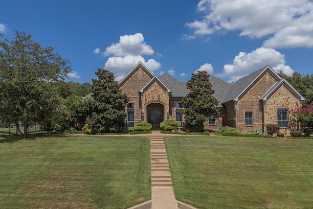 view of front of home with stone siding, brick siding, a front yard, and a shingled roof