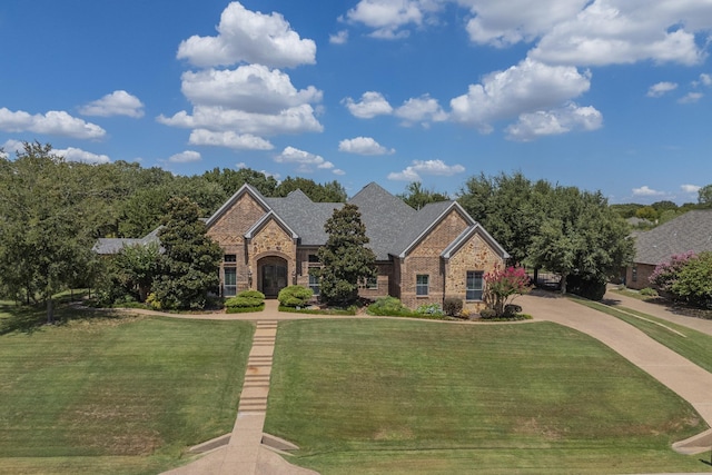 view of front facade with brick siding, roof with shingles, and a front yard