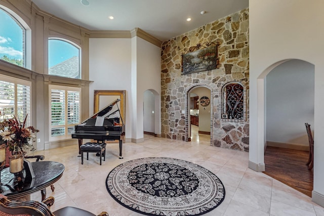 living area featuring crown molding, baseboards, a high ceiling, light tile patterned flooring, and arched walkways