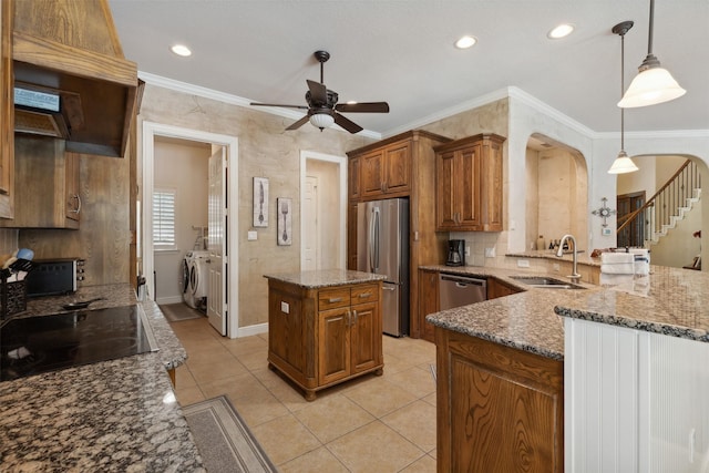 kitchen featuring brown cabinetry, arched walkways, a sink, appliances with stainless steel finishes, and washer and clothes dryer