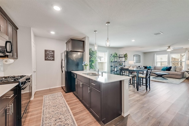 kitchen with a sink, black gas range oven, light countertops, and light wood finished floors