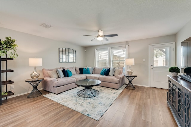 living room with light wood-style floors, visible vents, and baseboards