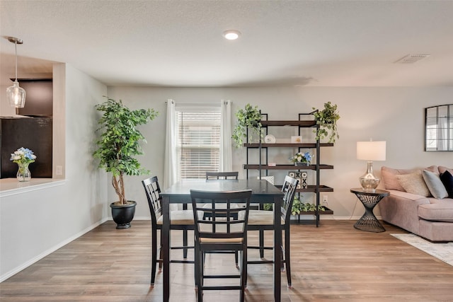 dining space featuring light wood-style flooring, baseboards, visible vents, and a textured ceiling