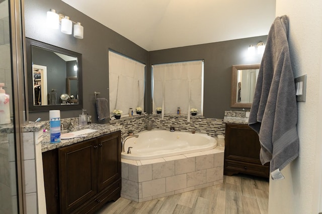 full bathroom featuring vanity, lofted ceiling, wood finished floors, and a tub with jets