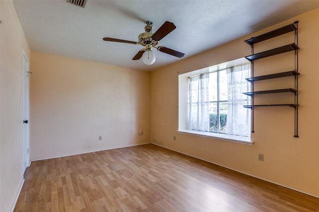 unfurnished room with baseboards, wood finished floors, visible vents, and ceiling fan