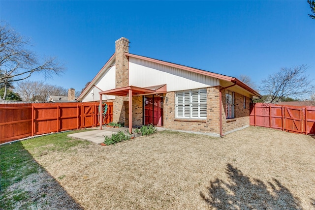 back of property with a patio, brick siding, a fenced backyard, and a chimney