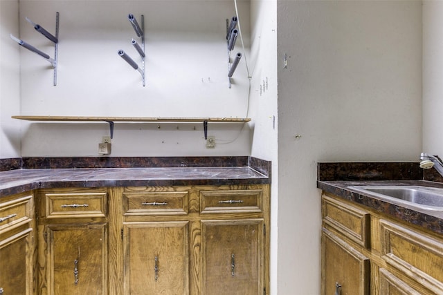 kitchen with brown cabinetry, dark countertops, and a sink