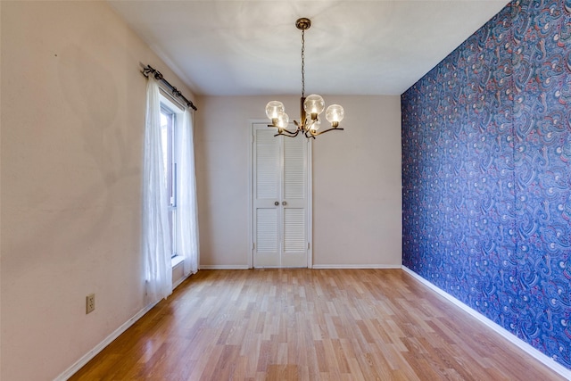 spare room with wallpapered walls, an accent wall, baseboards, a chandelier, and wood finished floors