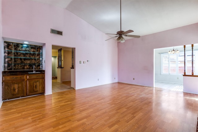 unfurnished living room with visible vents, ceiling fan with notable chandelier, light wood-style floors, high vaulted ceiling, and a sink