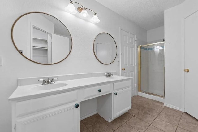 bathroom with double vanity, a shower stall, a textured ceiling, and a sink