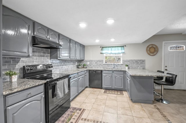 kitchen with black appliances, gray cabinets, under cabinet range hood, backsplash, and a peninsula