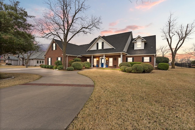 view of front facade featuring brick siding, a shingled roof, decorative driveway, and a front lawn