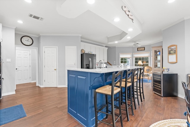 kitchen with wood finished floors, white cabinets, stainless steel fridge with ice dispenser, and visible vents