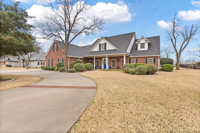 view of front of property with brick siding, a front lawn, roof with shingles, covered porch, and decorative driveway