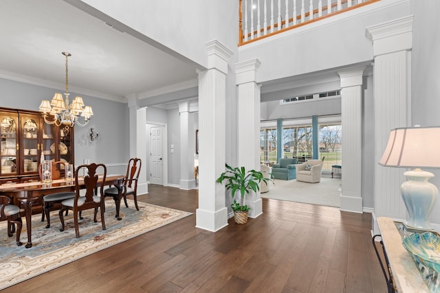 dining room with ornate columns, ornamental molding, dark wood-type flooring, a towering ceiling, and a notable chandelier