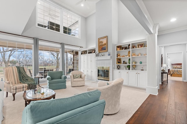 living room with a ceiling fan, a high ceiling, a fireplace, hardwood / wood-style flooring, and crown molding