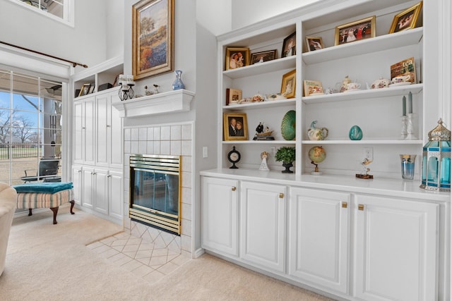 interior space with light carpet, a tiled fireplace, open shelves, white cabinetry, and light countertops