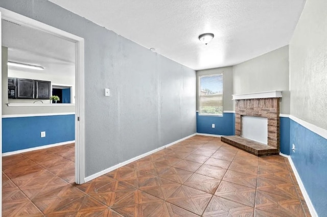 unfurnished living room featuring a brick fireplace, a textured wall, baseboards, and a textured ceiling