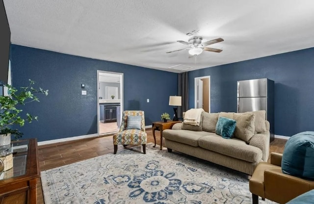 living area featuring a ceiling fan, a textured ceiling, wood finished floors, baseboards, and a textured wall