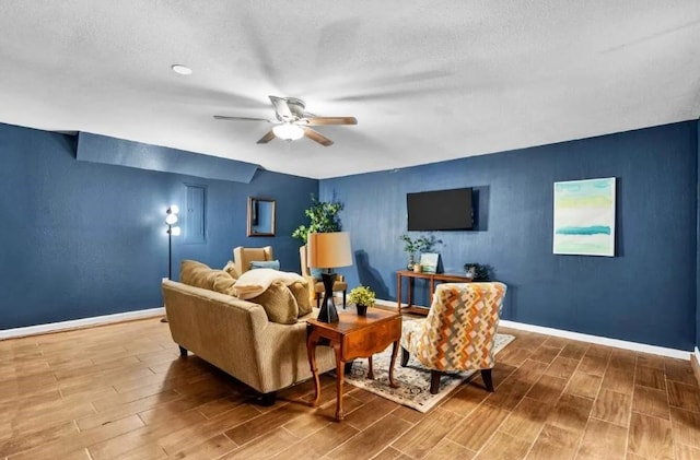 living room with ceiling fan, a textured ceiling, baseboards, and wood tiled floor