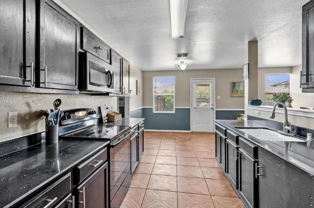 kitchen featuring stainless steel microwave, electric stove, light tile patterned flooring, a textured ceiling, and a sink