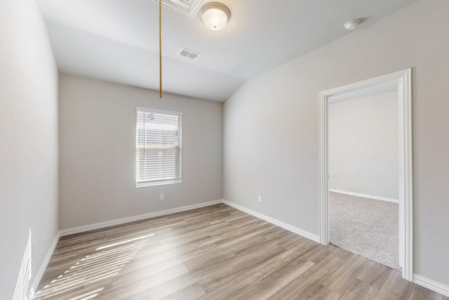 spare room with visible vents, baseboards, attic access, light wood-style flooring, and vaulted ceiling