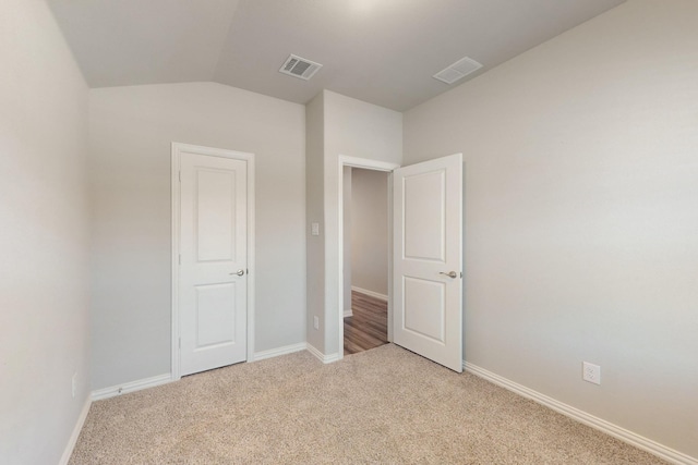 unfurnished bedroom featuring lofted ceiling, light colored carpet, visible vents, and baseboards