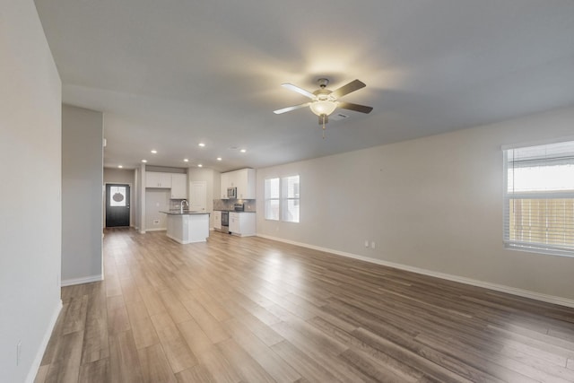 unfurnished living room featuring a ceiling fan, light wood-style floors, baseboards, and a sink