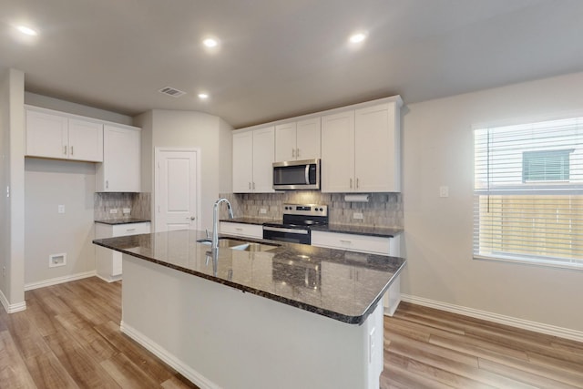 kitchen with visible vents, a kitchen island with sink, a sink, white cabinetry, and stainless steel appliances