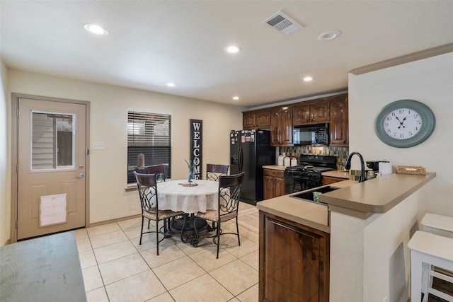 kitchen featuring visible vents, light tile patterned flooring, a sink, black appliances, and dark brown cabinetry