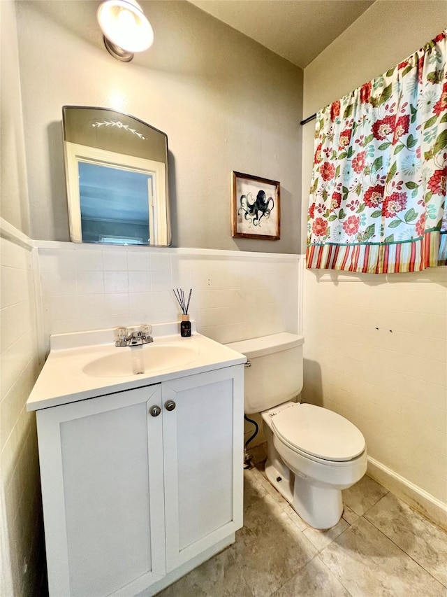 bathroom with vanity, tile patterned flooring, wainscoting, tile walls, and toilet