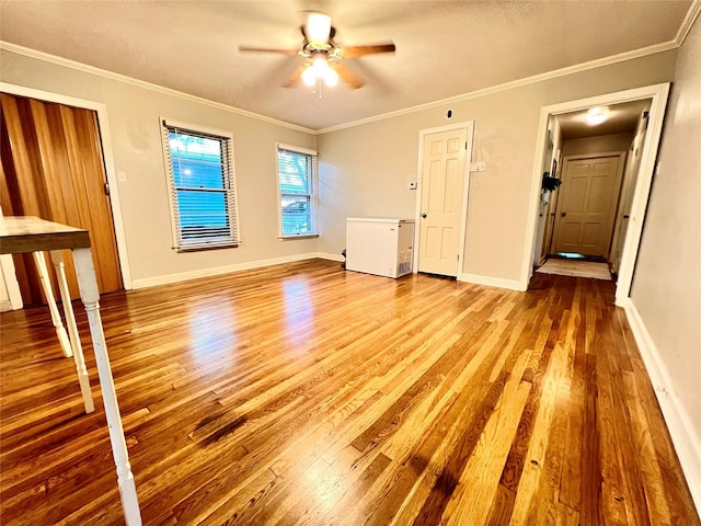 unfurnished living room with a ceiling fan, crown molding, baseboards, and wood finished floors