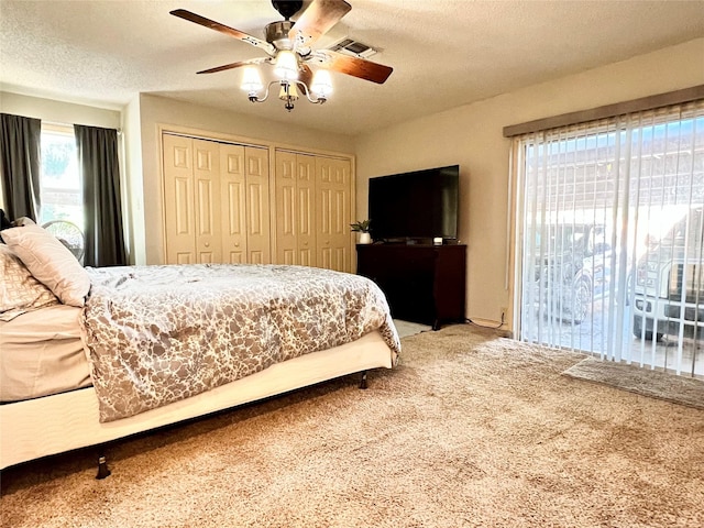 carpeted bedroom featuring visible vents, two closets, a ceiling fan, and a textured ceiling