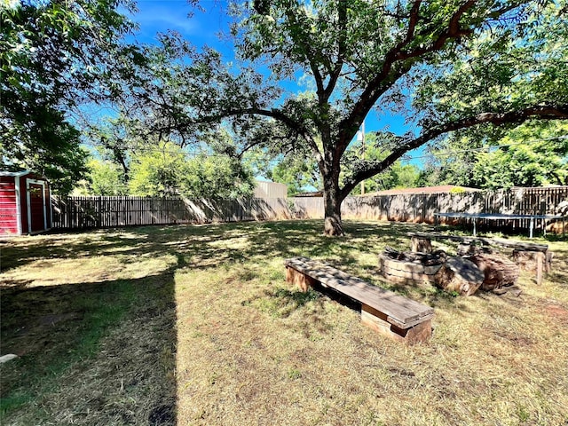 view of yard featuring an outbuilding, a trampoline, and a fenced backyard