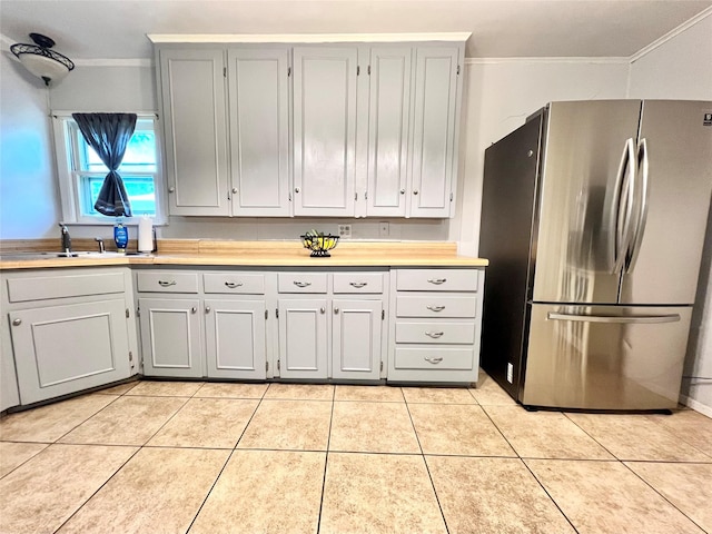 kitchen with light tile patterned flooring, freestanding refrigerator, a sink, gray cabinetry, and crown molding