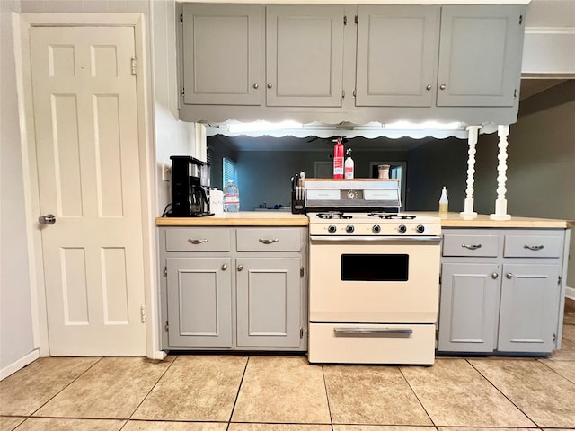 kitchen with light tile patterned flooring, gray cabinets, light countertops, and white range with gas stovetop