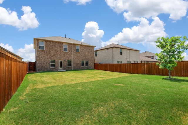 rear view of property featuring brick siding, a fenced backyard, and a yard