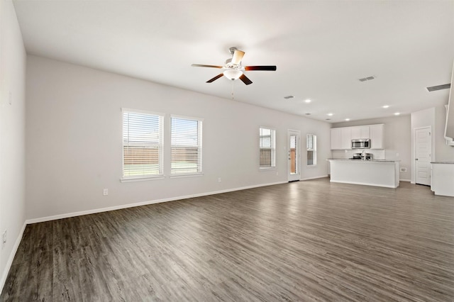 unfurnished living room with dark wood-style floors, visible vents, baseboards, and a ceiling fan