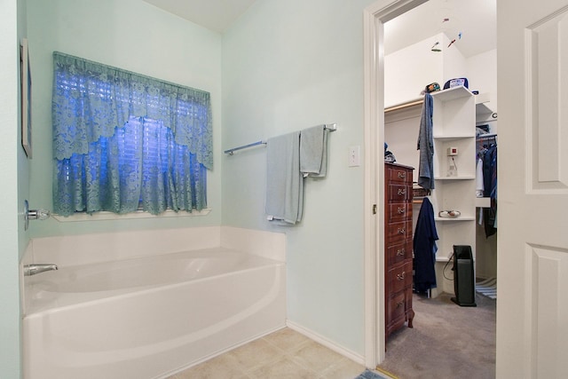 bathroom featuring a walk in closet, a garden tub, and baseboards