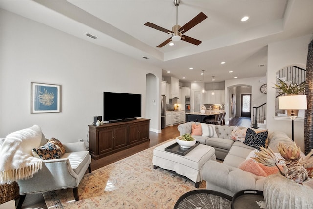 living room with wood finished floors, visible vents, arched walkways, stairs, and a raised ceiling