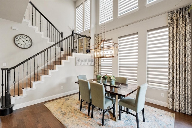 dining space with a chandelier, baseboards, a towering ceiling, and wood finished floors