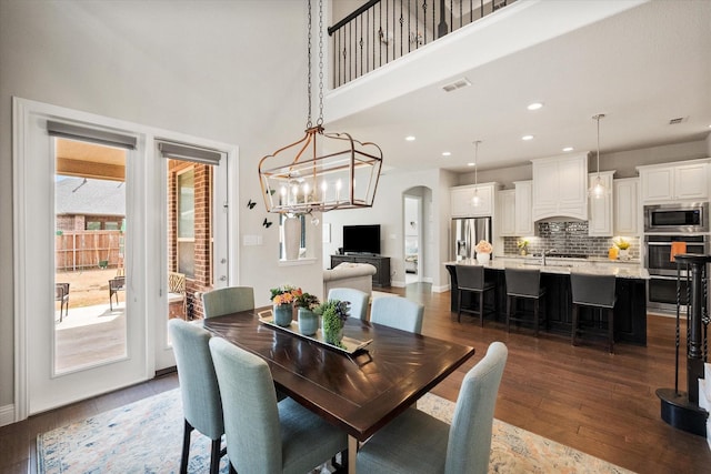 dining space featuring visible vents, wood finished floors, recessed lighting, arched walkways, and a towering ceiling