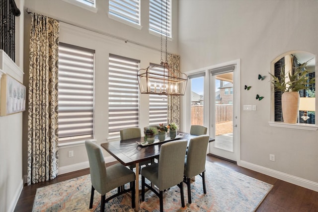 dining area featuring baseboards, a high ceiling, an inviting chandelier, and wood finished floors