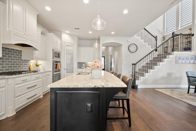 kitchen with a sink, arched walkways, appliances with stainless steel finishes, a breakfast bar area, and white cabinets