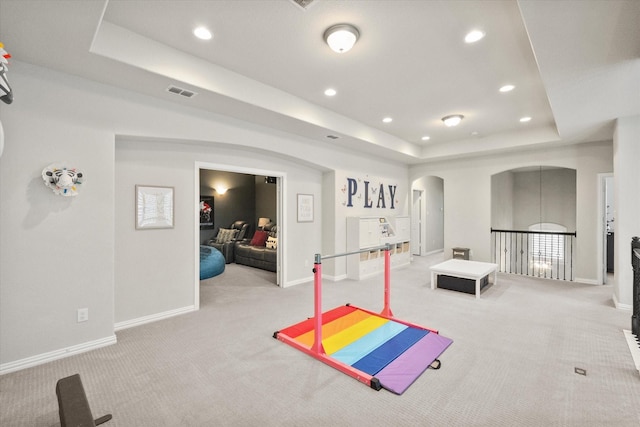 exercise room featuring arched walkways, visible vents, carpet, and a tray ceiling