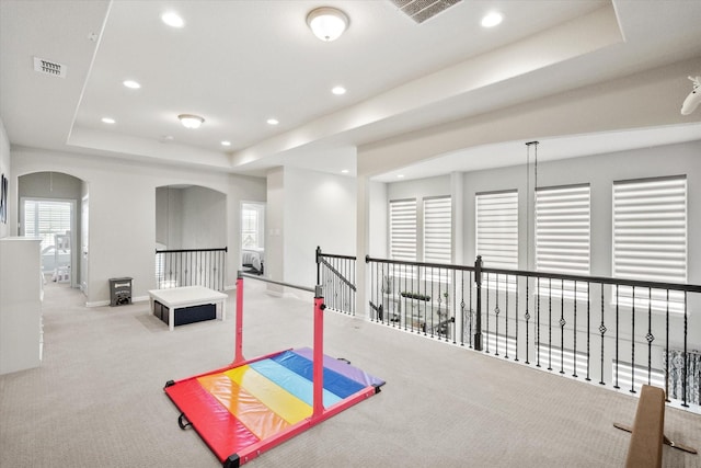 recreation room featuring visible vents, baseboards, a tray ceiling, carpet floors, and arched walkways